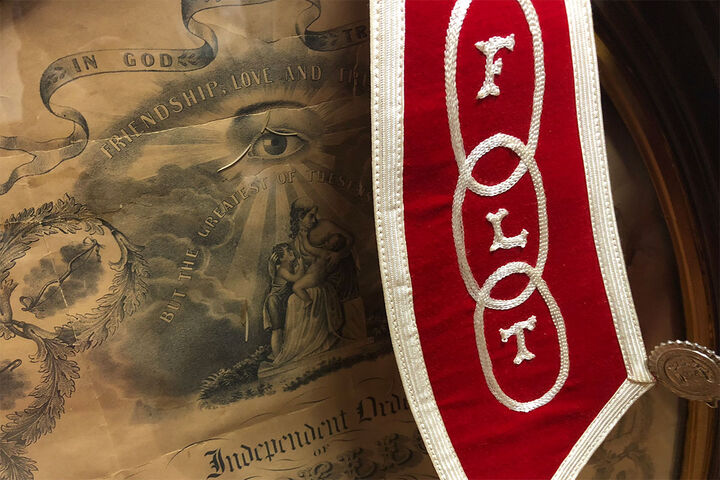 A poster for the Independent Order of Odd Fellows fraternal order and a red stole embroidered with the letters F, L, and T.